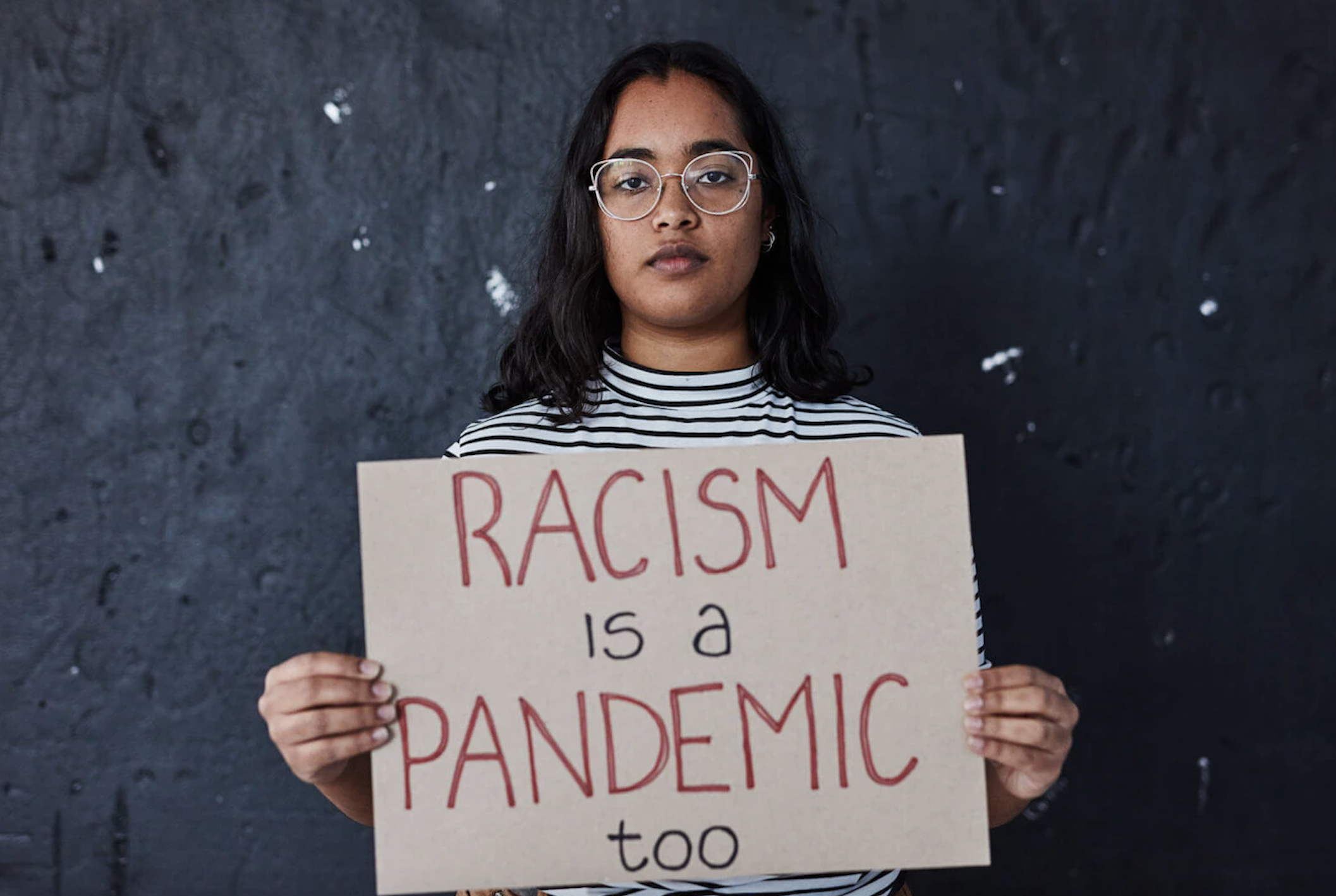 Person holding cardboard sign that reads "racism is a pandemic too"
