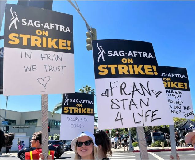 Close up of four picket signs being held aloft by picketers. Text on signs: "In Fran We Trust" (with a heart) and "Fran Stan 4 Lyfe"