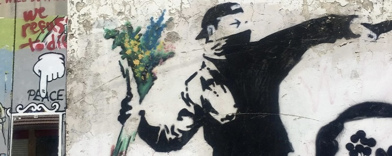 Art work by the artist Banksy on the West Bank Apartheid Wall. The graffiti is of a man with his face covered throwing flowers towards the other side.