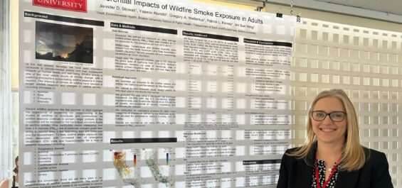 Dr. Jennifer Stowell standing in front of her poster 'Differential Impacts of Wildfire Smoke Exposure in Adults' at the ISES conference.
