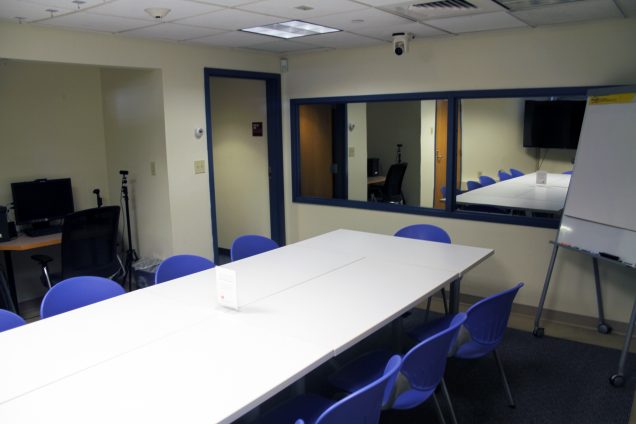 An image of a rectangular table lined with chairs, a one-way mirror lines the back wall.