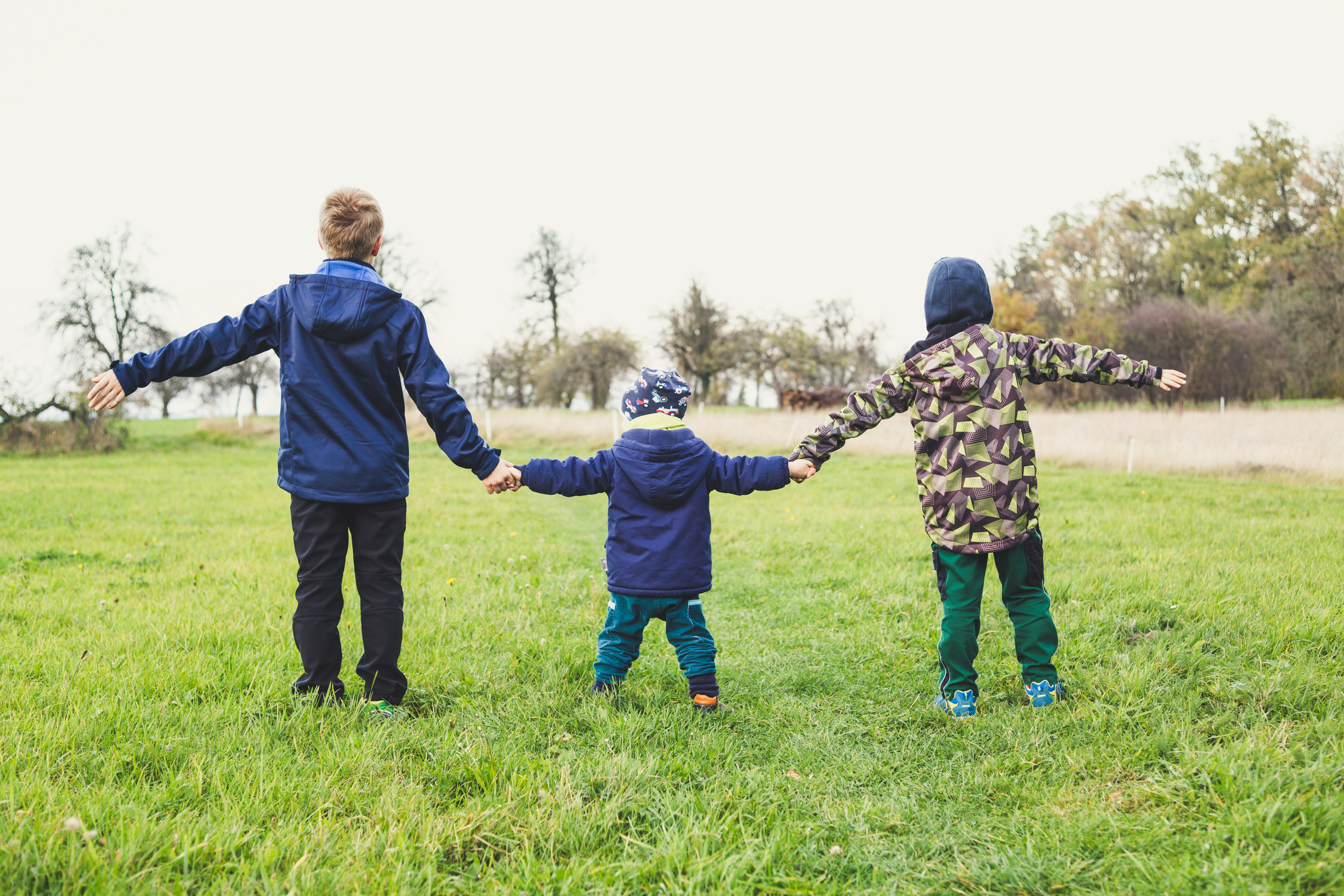 Three children holding hands standing on grass