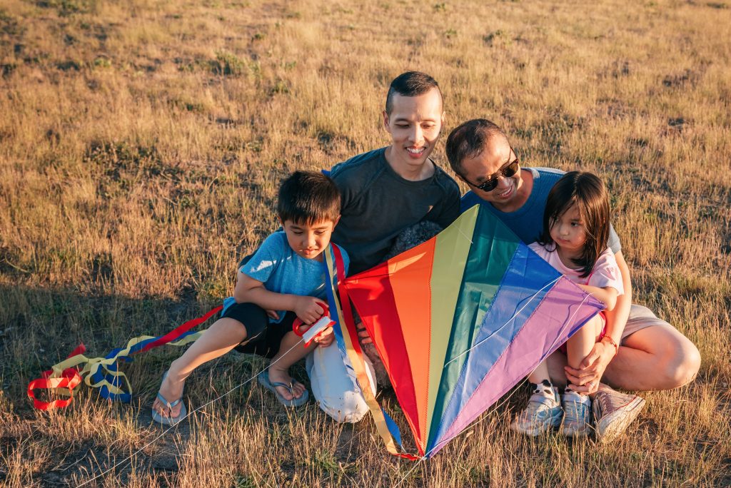 family with children outside seated in the grass with a kite