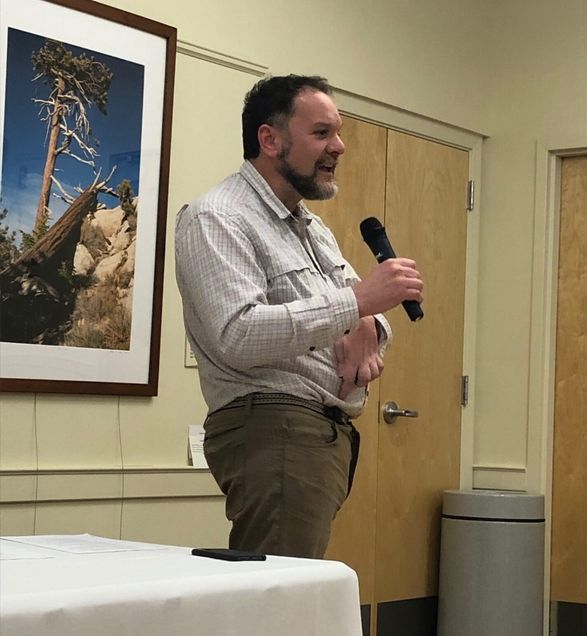 Artist Dan Wells holds a microphone as he presents with one of his photos of a tree behind him.