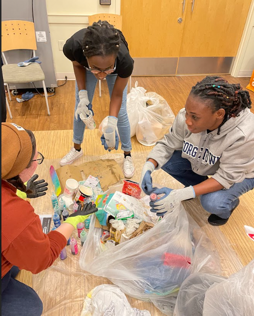 Three students sorting through the trash and recycling. Each are wearing gloves and looking at each other.