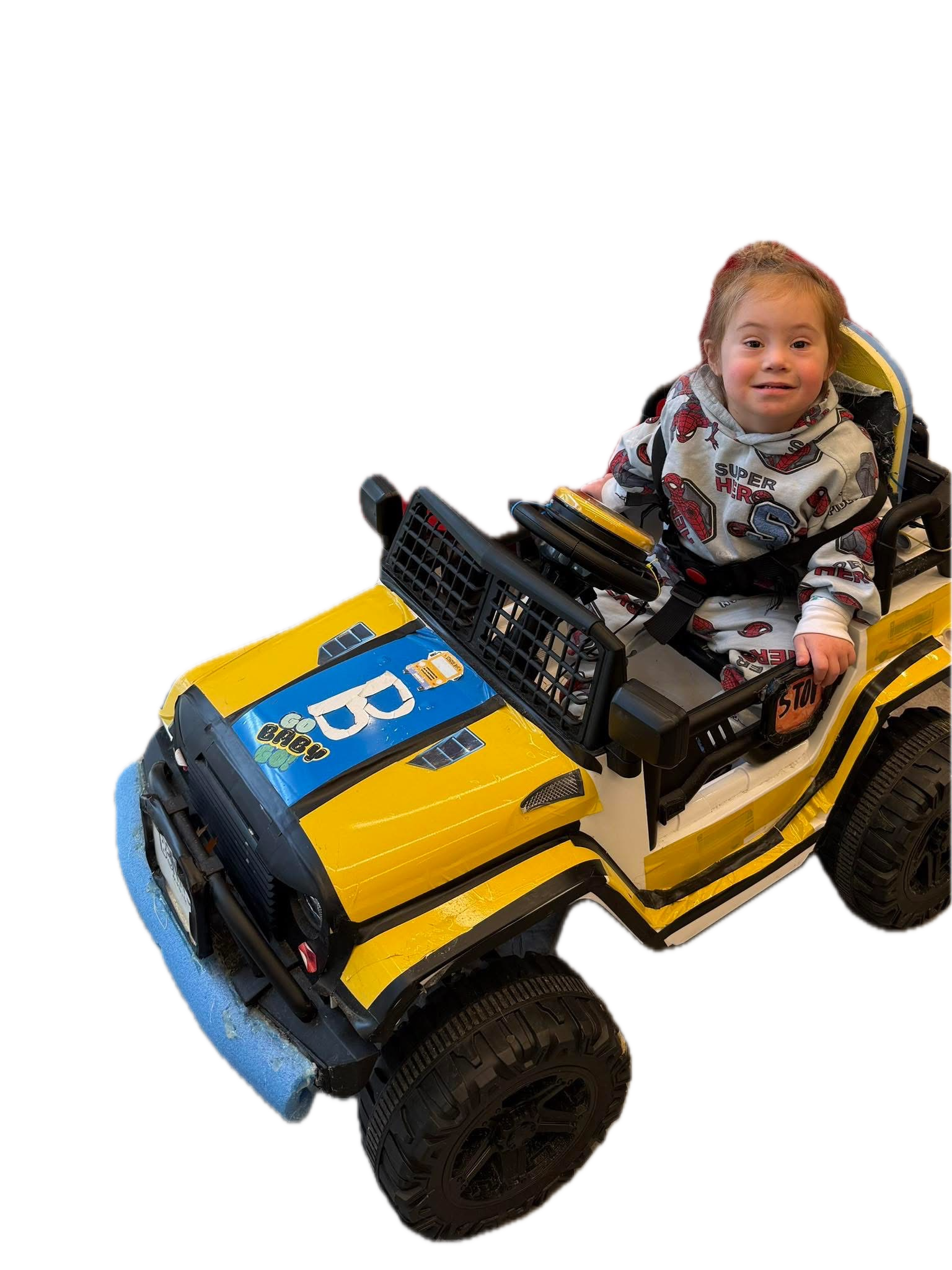 A smiling child rides a yellow Go Baby Go modified ride-on car