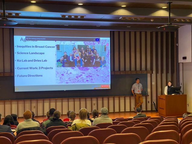 Dr Ko and Dr Dries presenting their talk in an auditorium with a presentation on the screen behind them