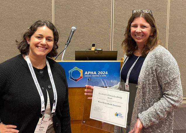 Candice Bangham and Rebecca Boulos posing with an Excellence in Climate Leadership Award in front of a podium at APHA