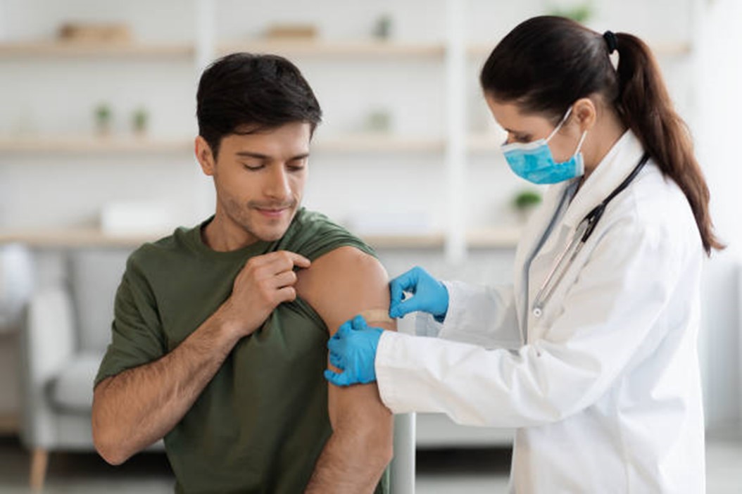 Healthcare professional administering a vaccine to a patient, who is rolling up their sleeve