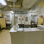 Interior of an overdose prevention center with individual numbered booths, harm reduction supplies, and a sign reading 'This Site Saves Lives' in English and Spanish.