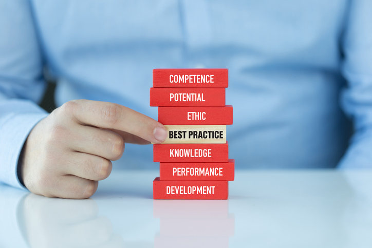 A person points to a stack of red wooden blocks labeled with professional development terms including Competence, Potential, Ethic, Best Practice, Knowledge, Performance, and Development.