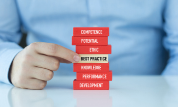 A person points to a stack of red wooden blocks labeled with professional development terms including Competence, Potential, Ethic, Best Practice, Knowledge, Performance, and Development.