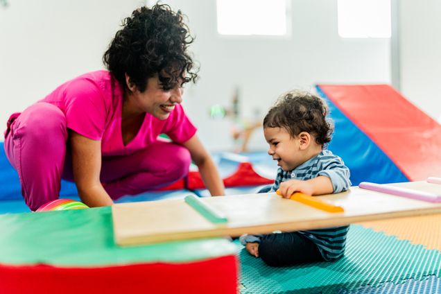 Young teacher playing with baby boy at playroom