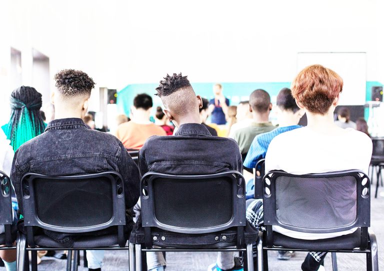 Photo of students sitting in a classroom seen from behind the students with an instructor in the background.